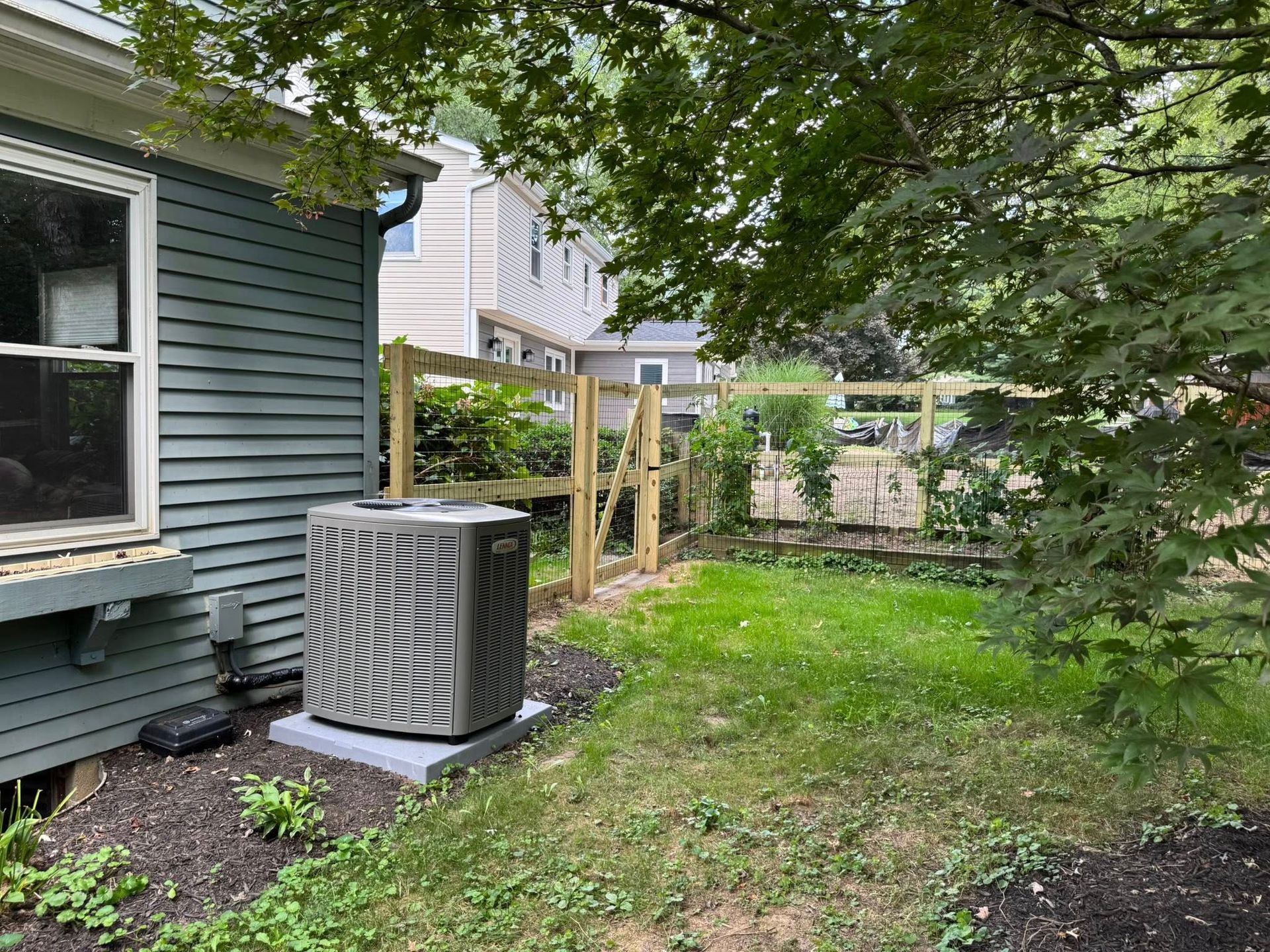 Backyard with AC unit, green siding, wooden fence, and grassy area.