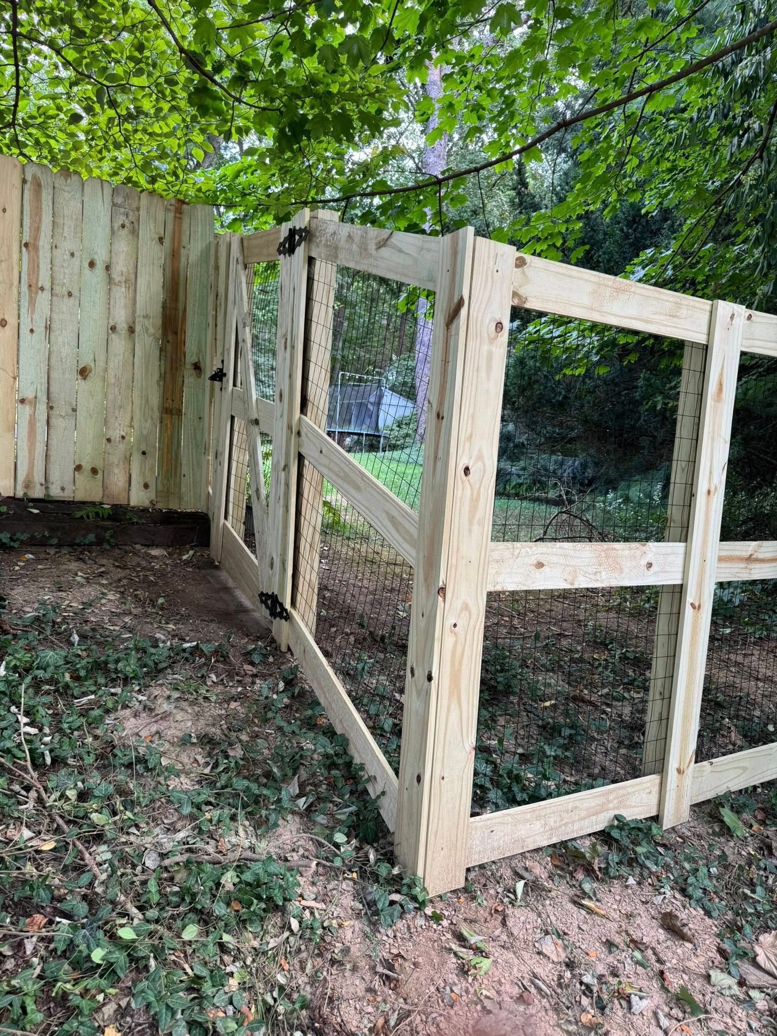 Wooden fence with a gate in a grassy, wooded area.