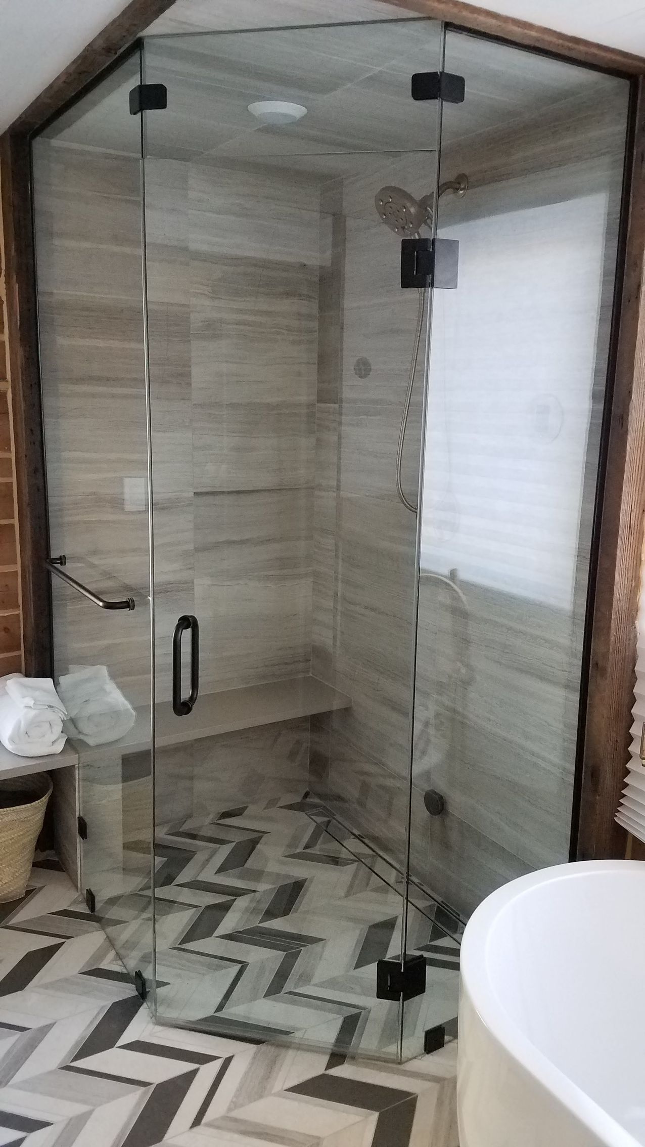 A modern, angled glass shower with a black handle and fixtures. The shower is tiled and has a bench.