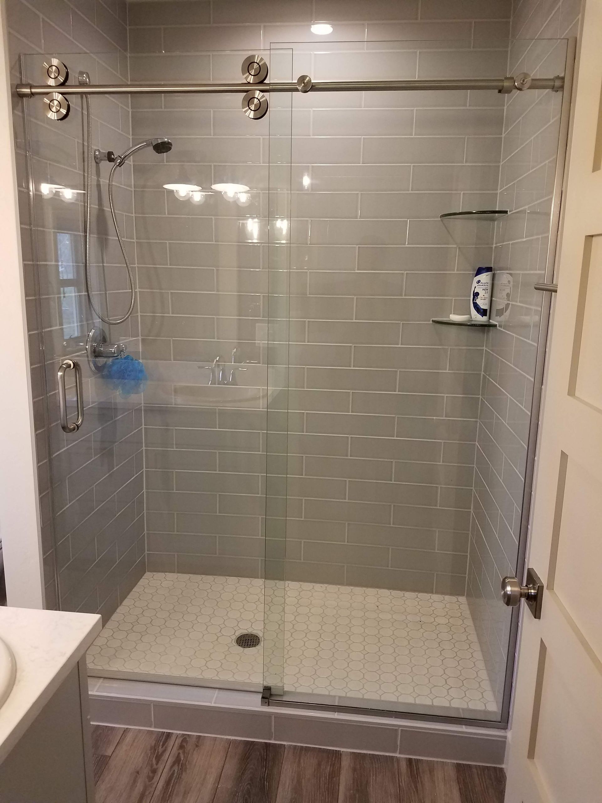A modern, tiled shower with a sliding glass door, gray walls, and a stone floor. Chrome hardware