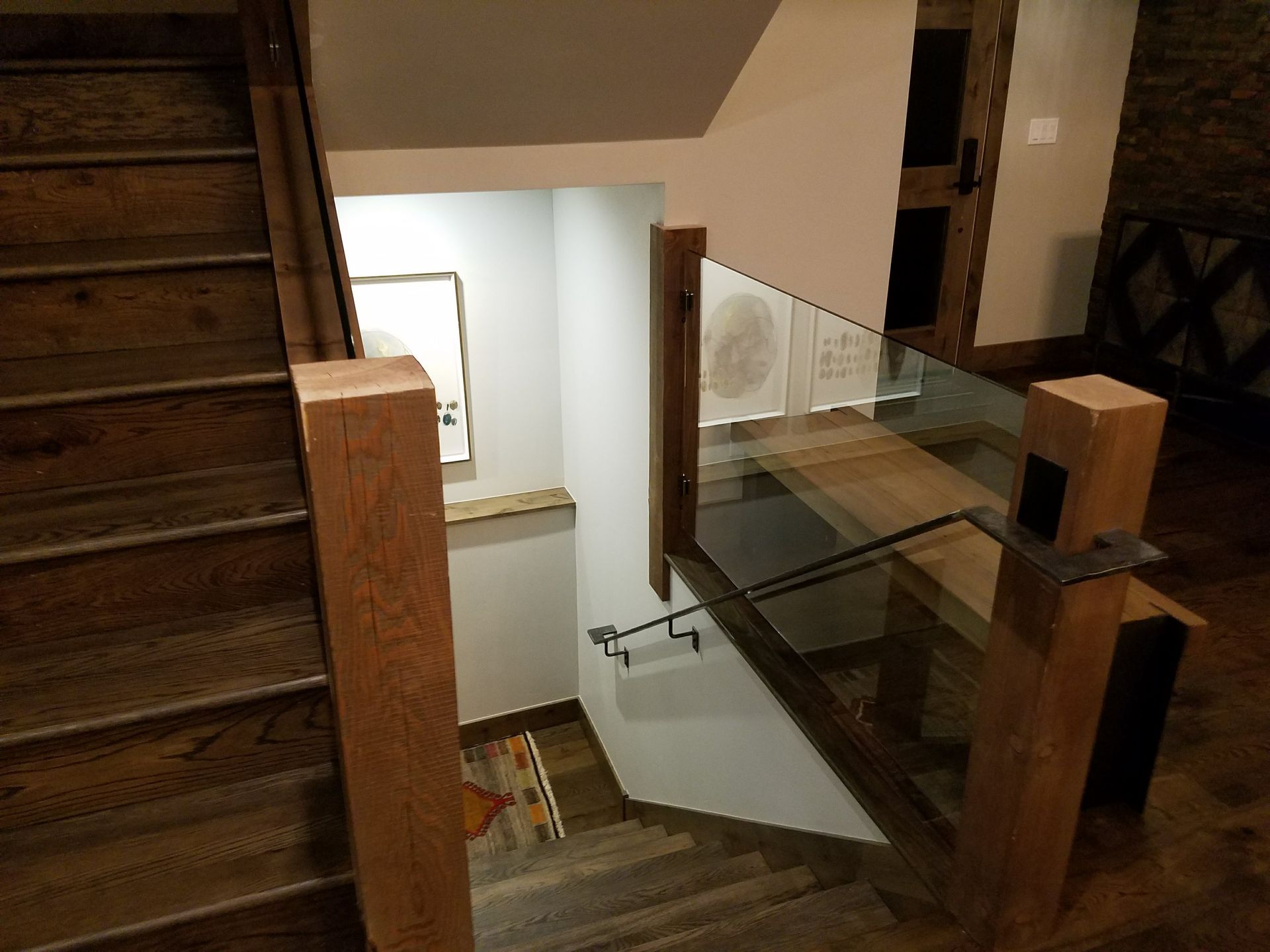 Wooden staircase descending into a lower level. The staircase has a glass and wood railing