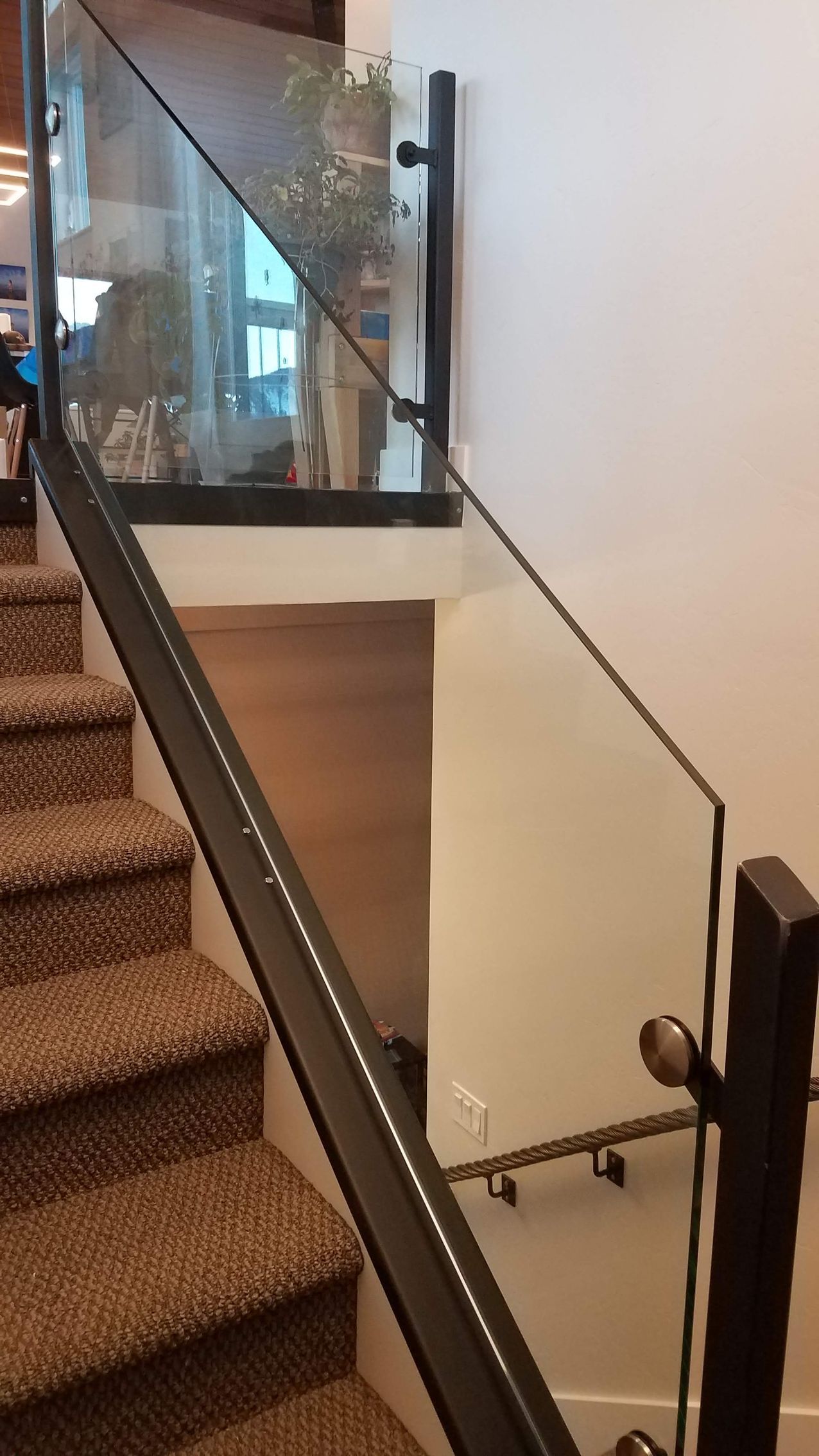 Staircase with brown carpet and glass railing, black metal frame. 