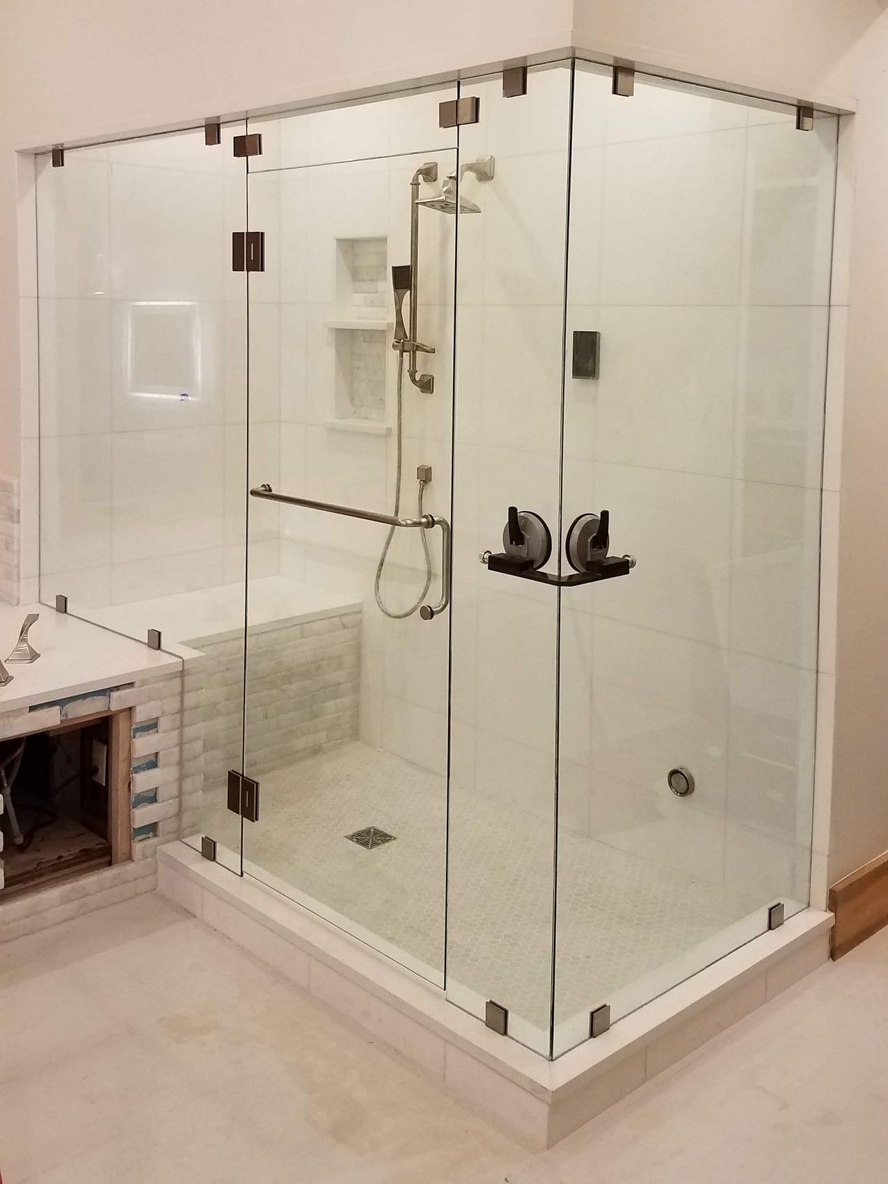 A modern, glass-enclosed shower with chrome fixtures, white walls, and a mosaic tile accent.