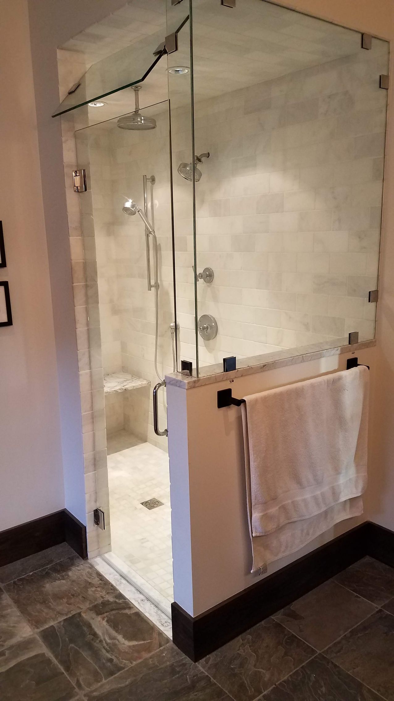 Glass-enclosed shower in a bathroom with a towel rack. The shower has a built-in bench and chrome fixtures.