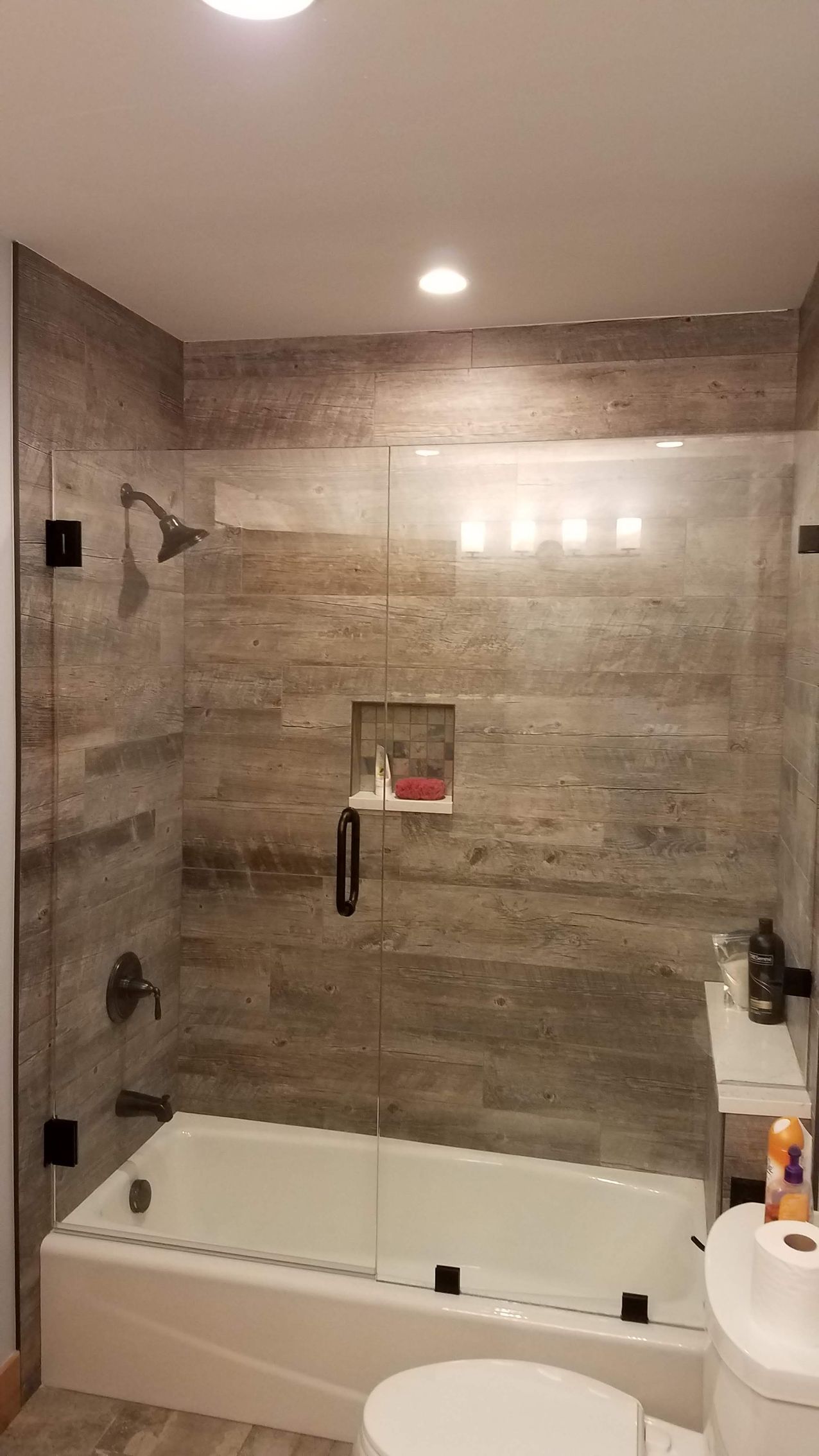 A modern bathroom with a tiled shower over a bathtub. Glass panels enclose the shower