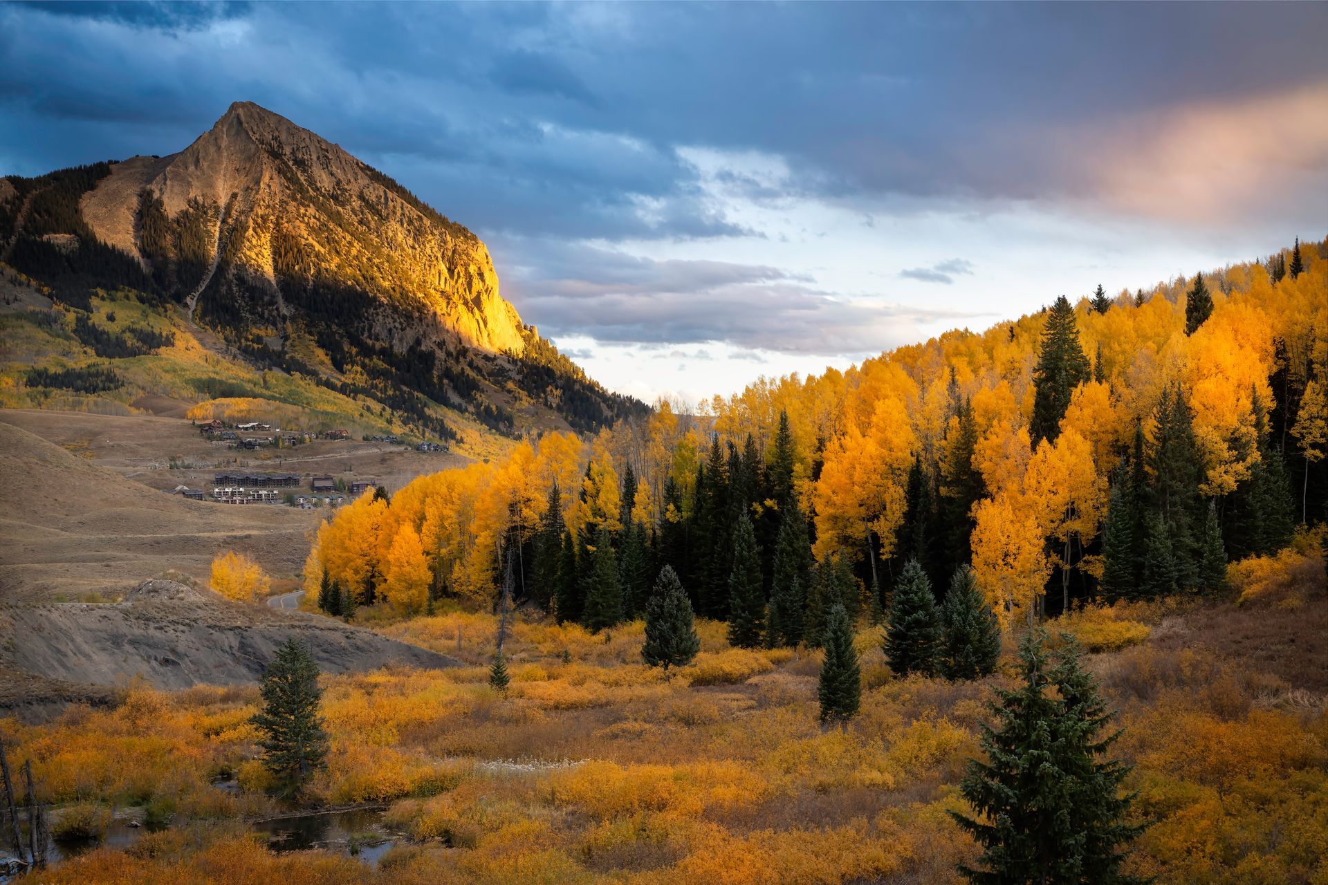 Mountain landscape with golden autumn trees and a peak lit by sunlight.