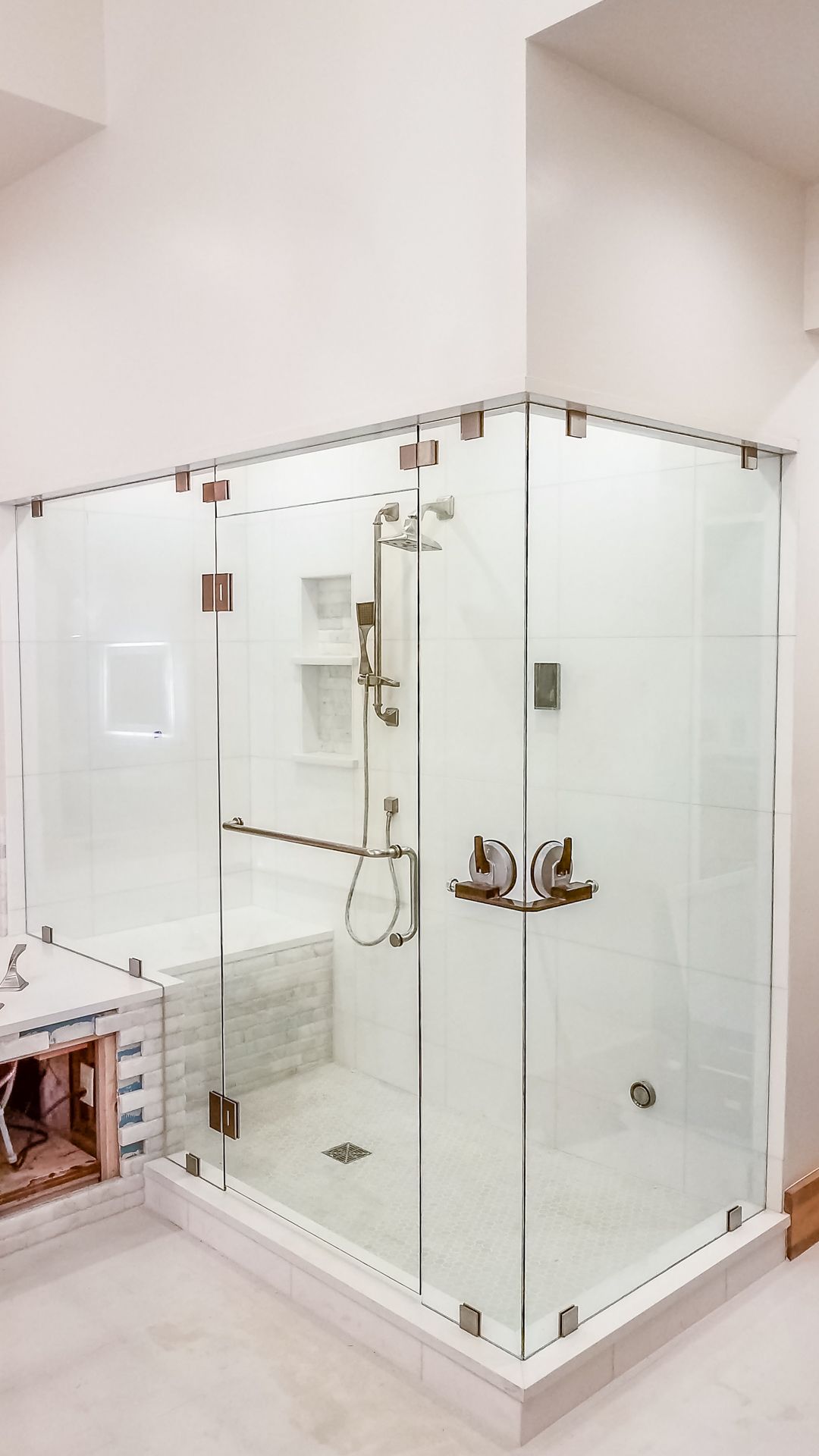 A modern, glass-enclosed shower with chrome fixtures and a white tile base, set in a bright, white bathroom.