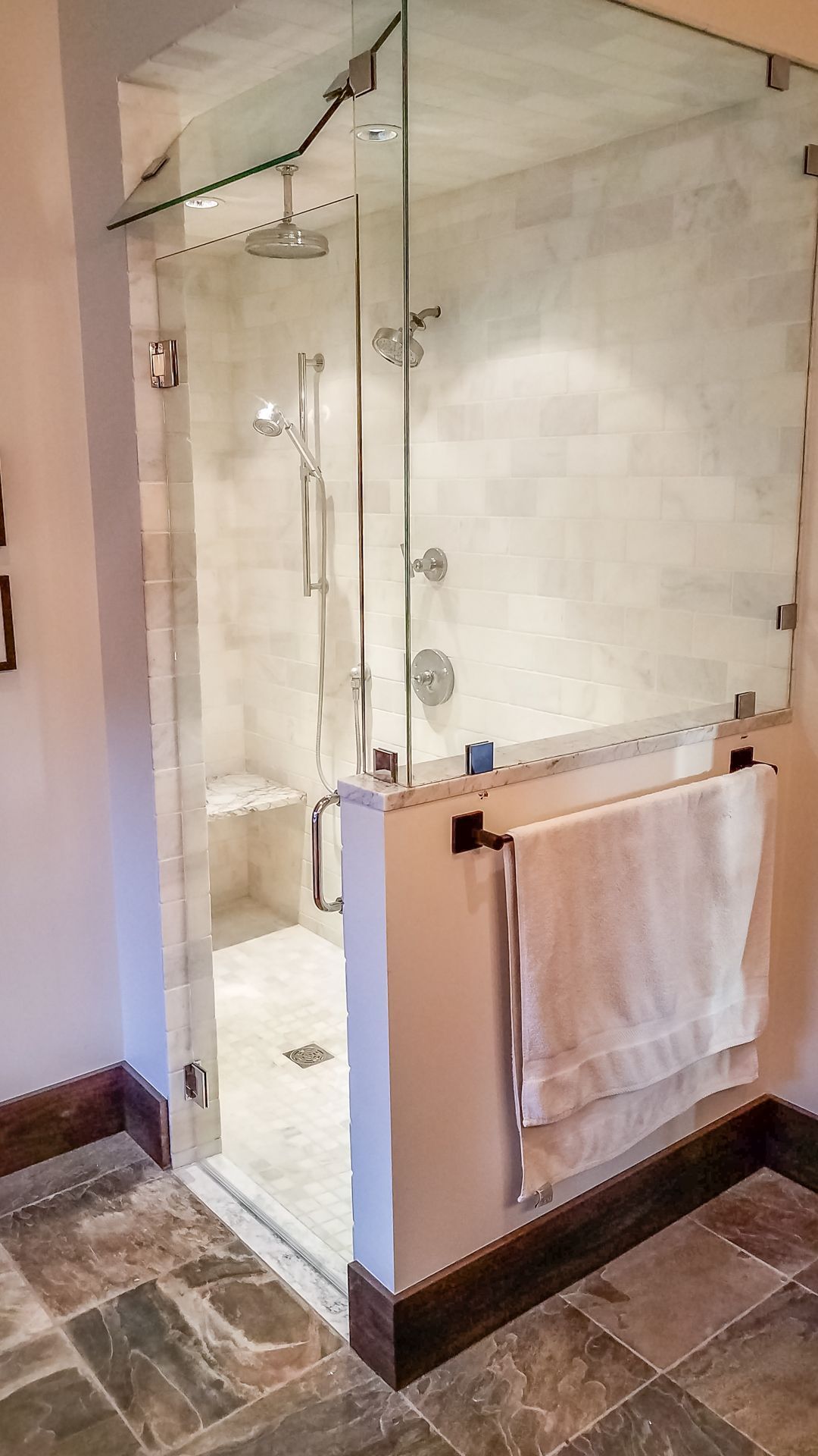 A glass-enclosed shower with white tile interior. A white towel hangs on a bar outside the shower, set against a tile floor.