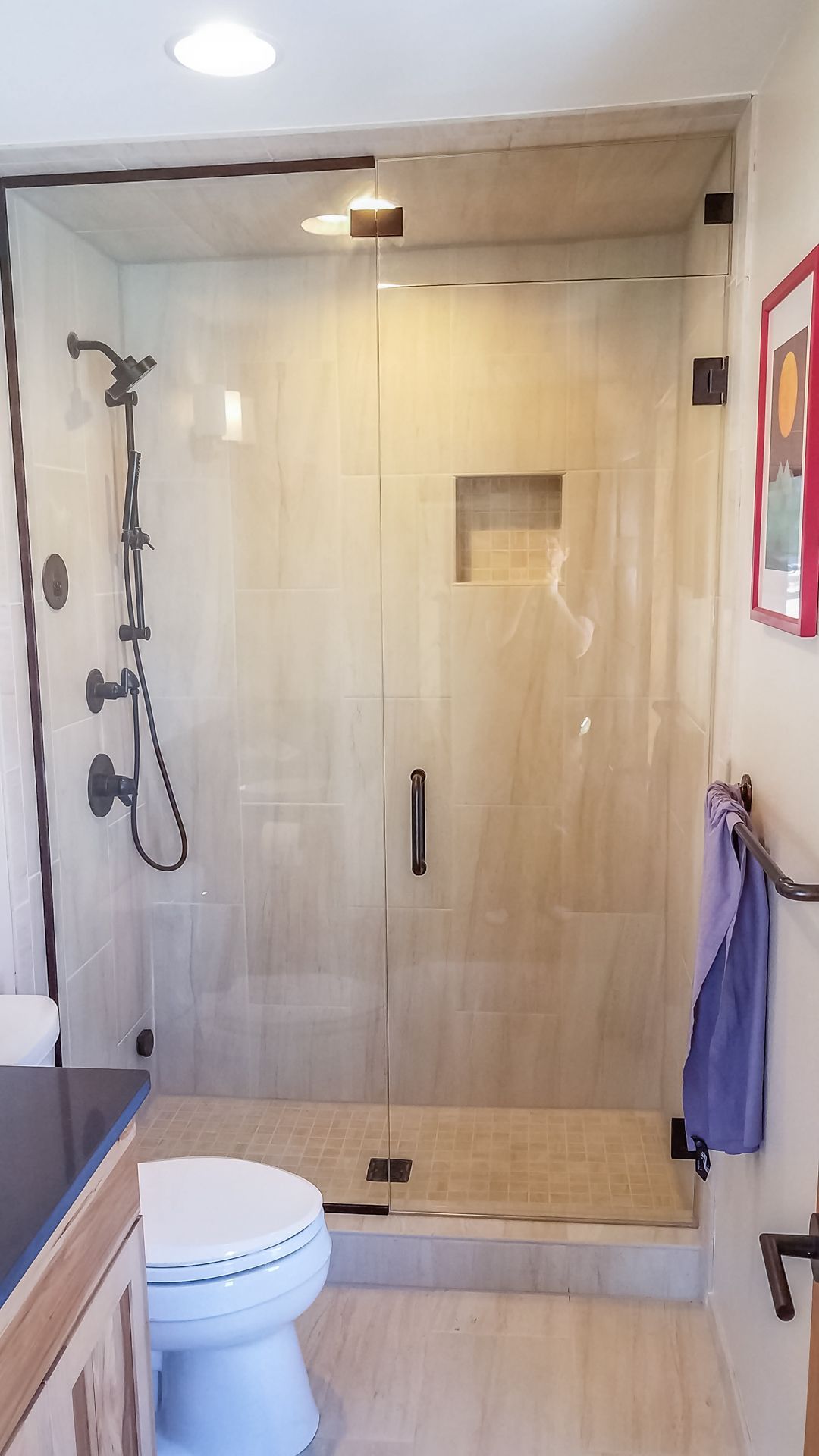 A bathroom with a frameless glass shower enclosure. Light-colored tile covers the walls and floor.