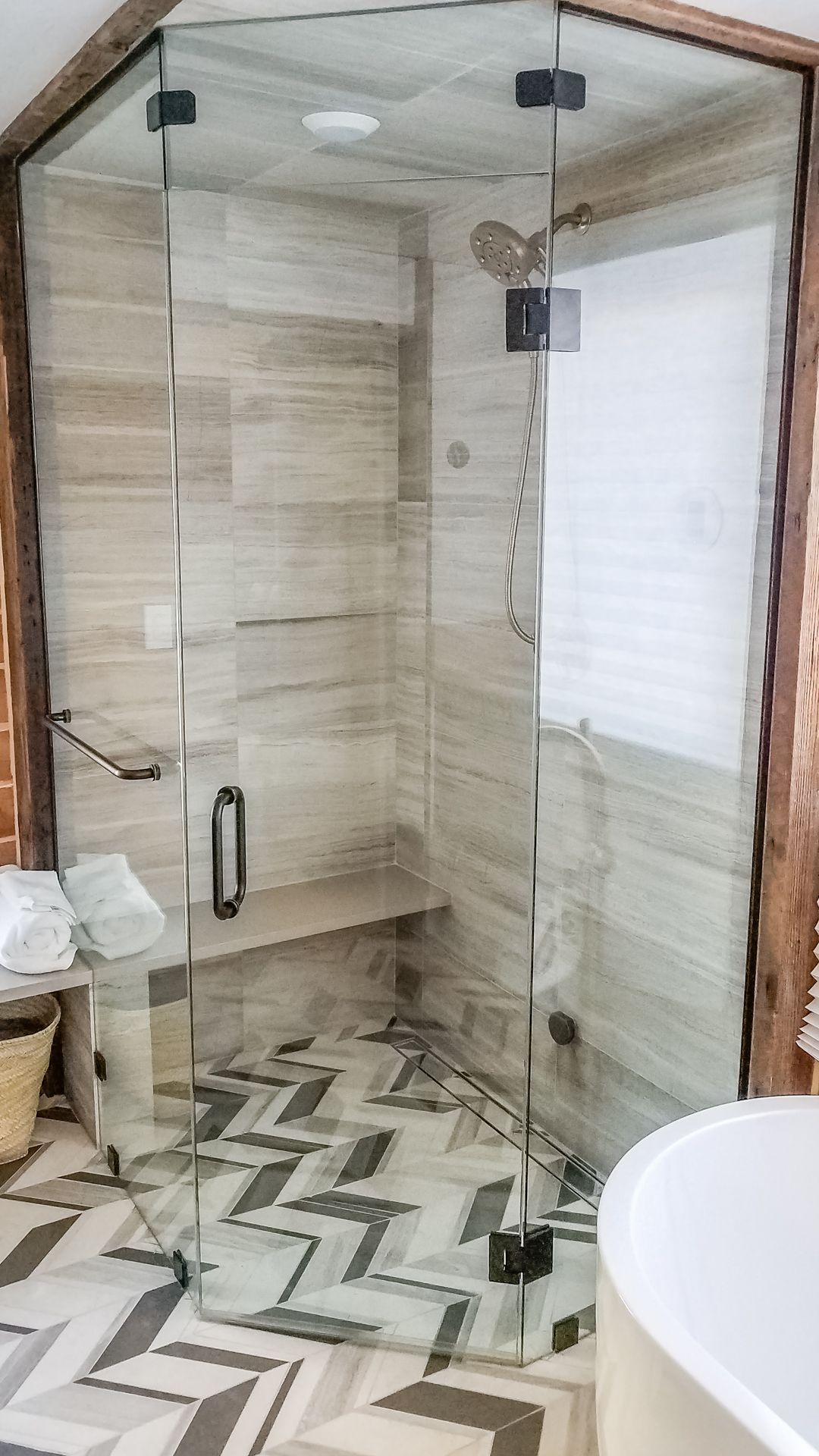 Modern glass shower with beige tiled walls, chevron patterned floor, and a built-in bench.