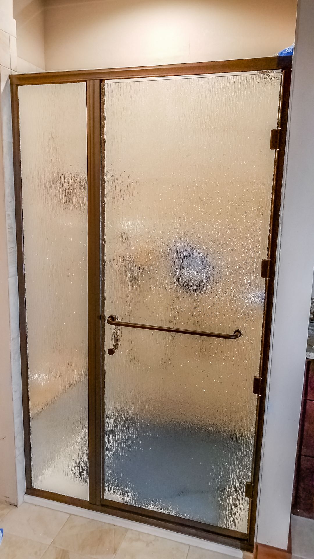 A frosted glass shower enclosure with a bronze frame. A long, dark handle is mounted on the sliding door.