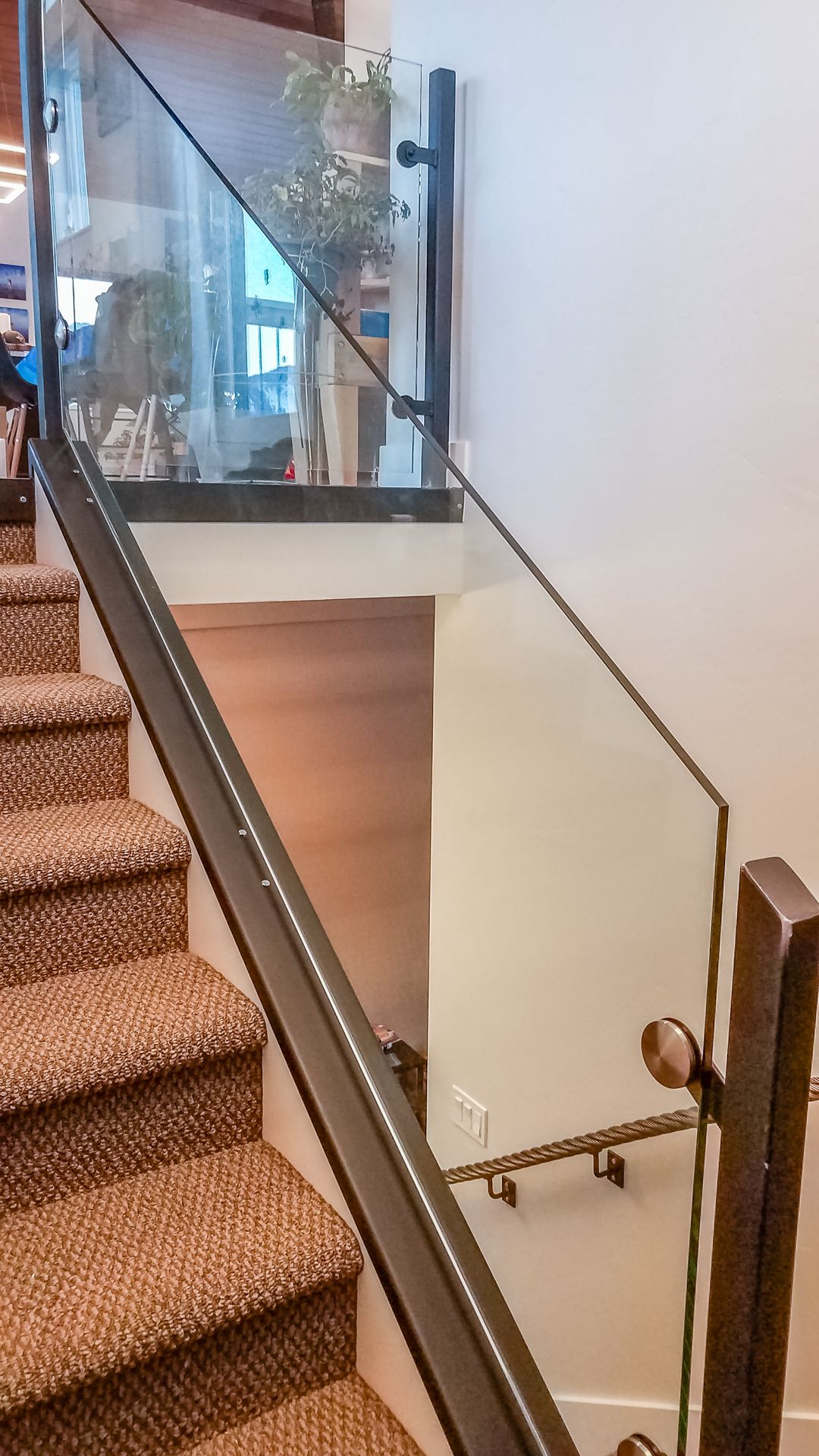 Staircase with carpeted steps and a glass railing with a dark metal frame. The railing continues onto a landing.