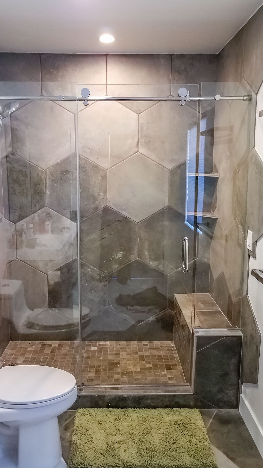 Bathroom with a glass-enclosed shower featuring hexagon-shaped tiles in various shades of gray, a built-in bench