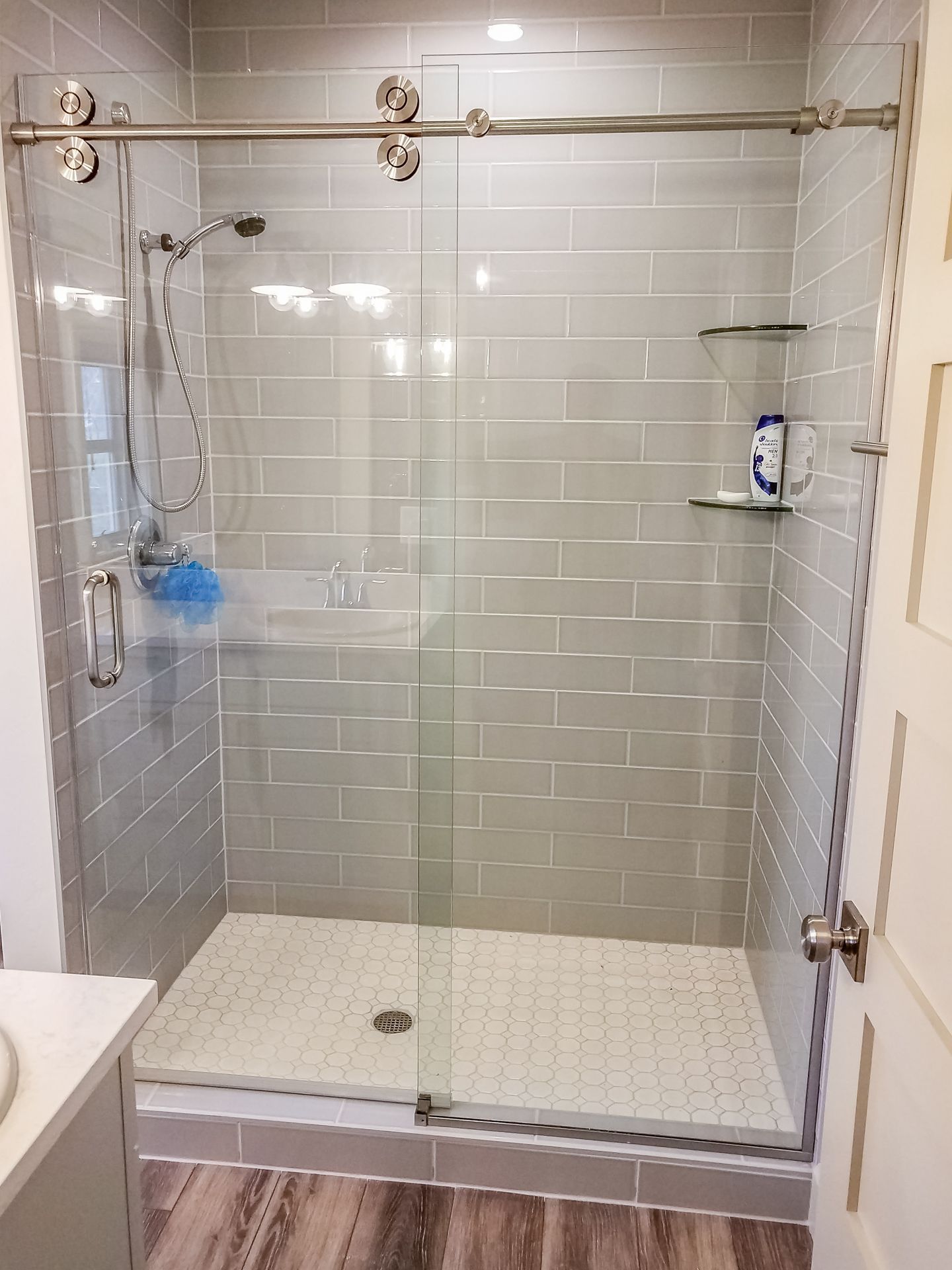 Modern bathroom with a gray-tiled shower. A glass door slides on a metal track.
