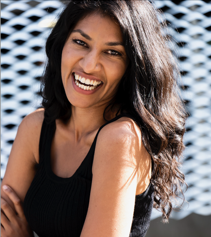 Smiling woman with long dark hair in a black top, standing before a patterned background.