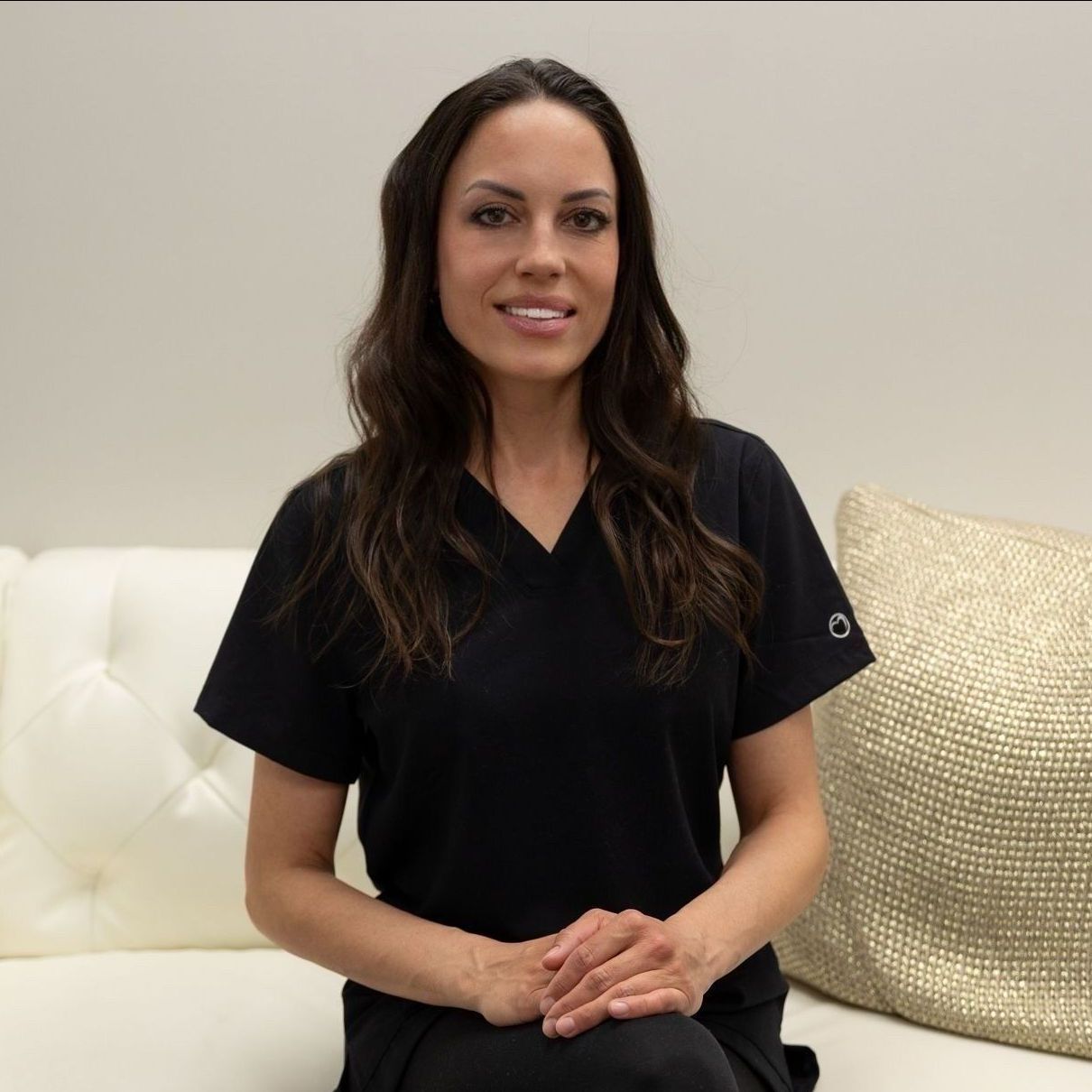 A woman in a black scrub top sits on a white couch
