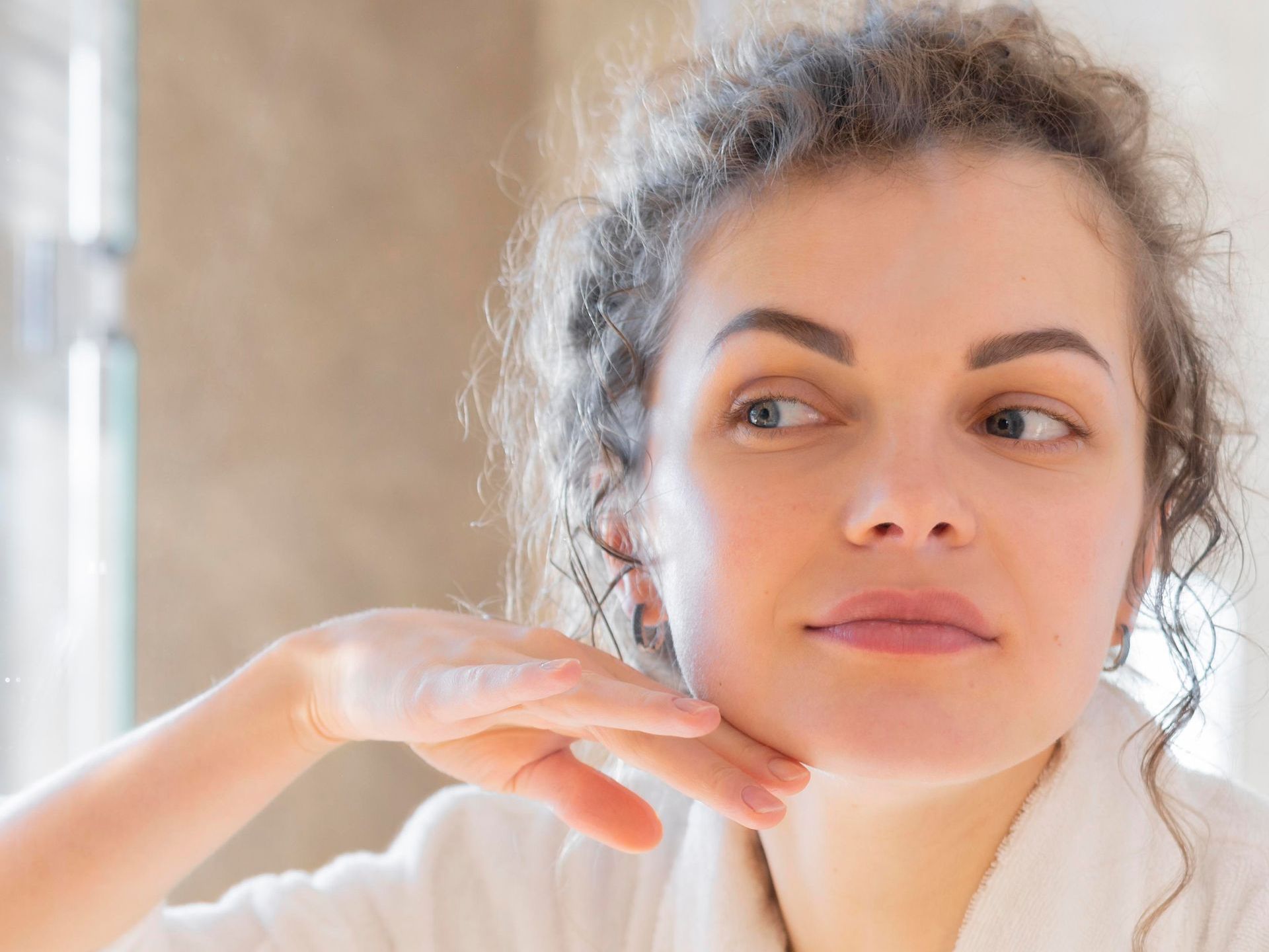 A woman is looking at her face in the mirror.