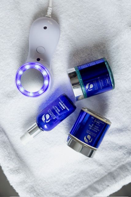 Three bottles of cosmetics and a device on a towel.