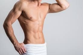 A shirtless man wrapped in a white towel is standing with his hands on his hips.