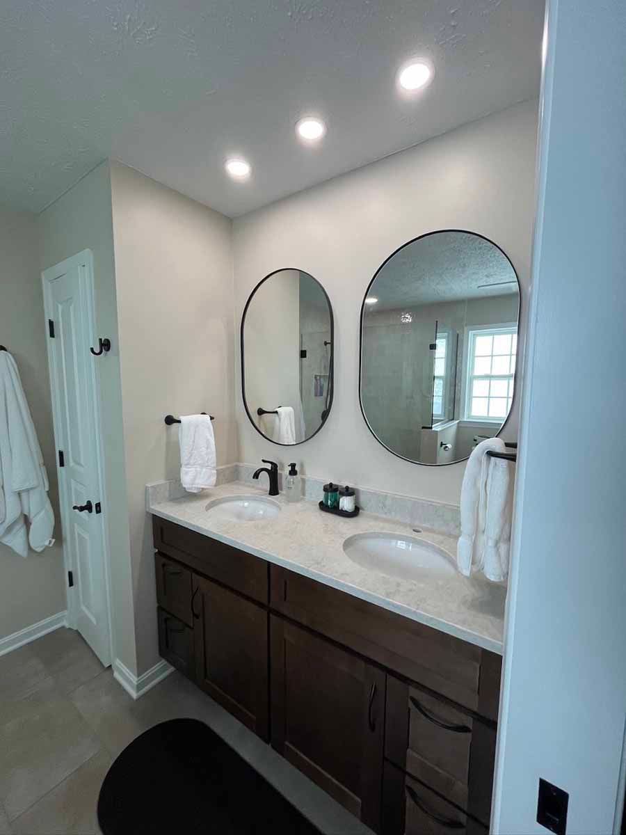 Bathroom with double sinks, oval mirrors, dark cabinets, and white towels.