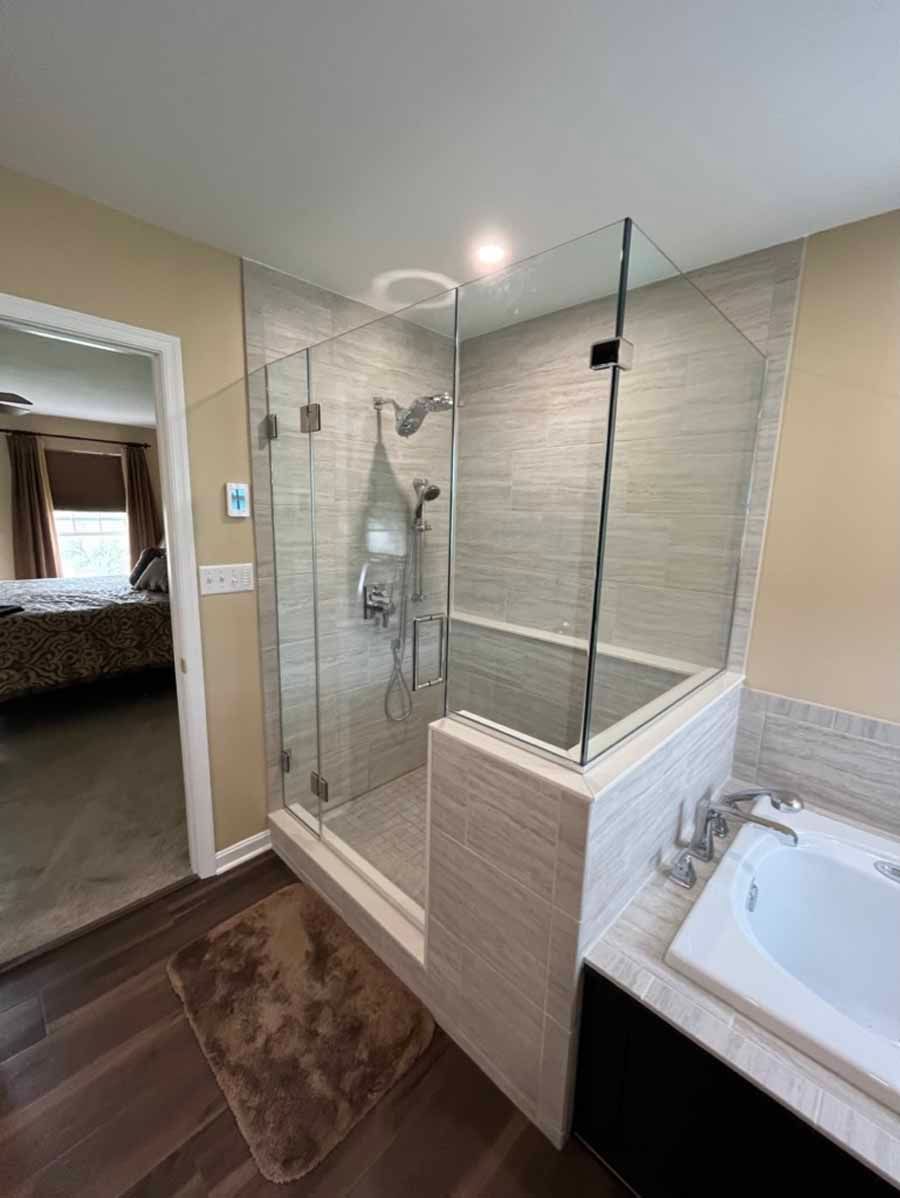 Modern bathroom with a glass shower, light gray tile, and a bathtub.