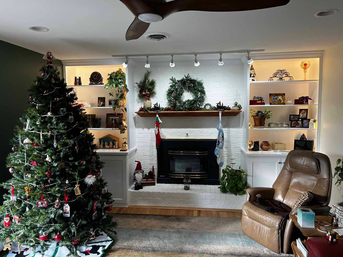 Christmas tree next to fireplace with decorations and a recliner in a living room.