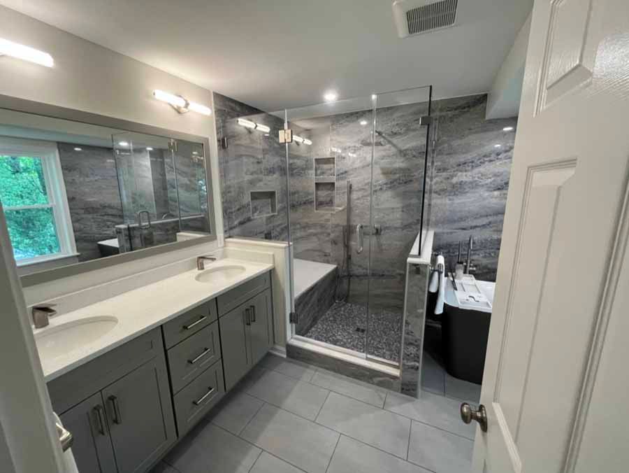 Newly renovated bathroom with gray and white tones, featuring double vanity, large shower, and soaking tub.