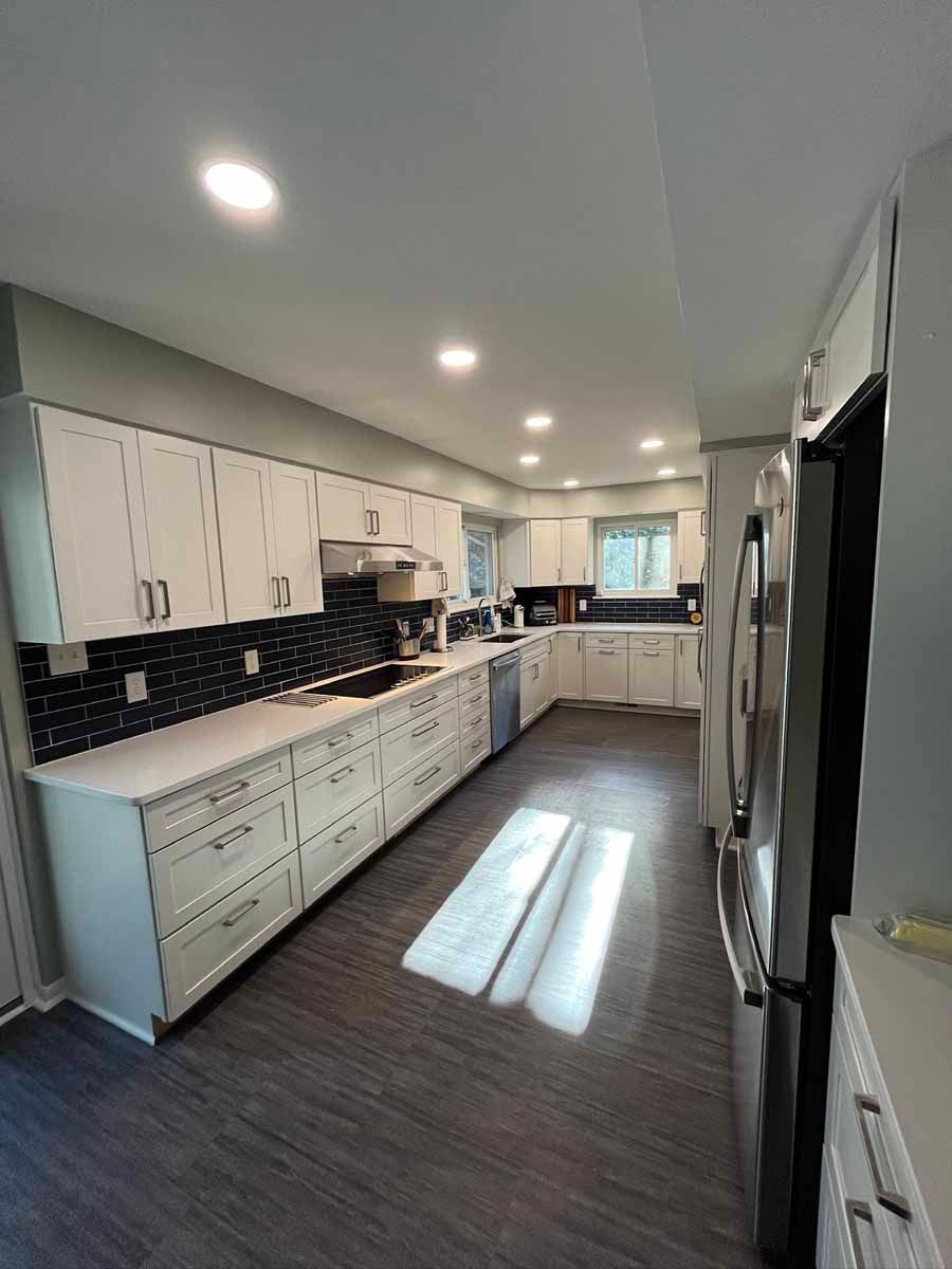Modern white kitchen with dark countertops and flooring; appliances and cabinets.