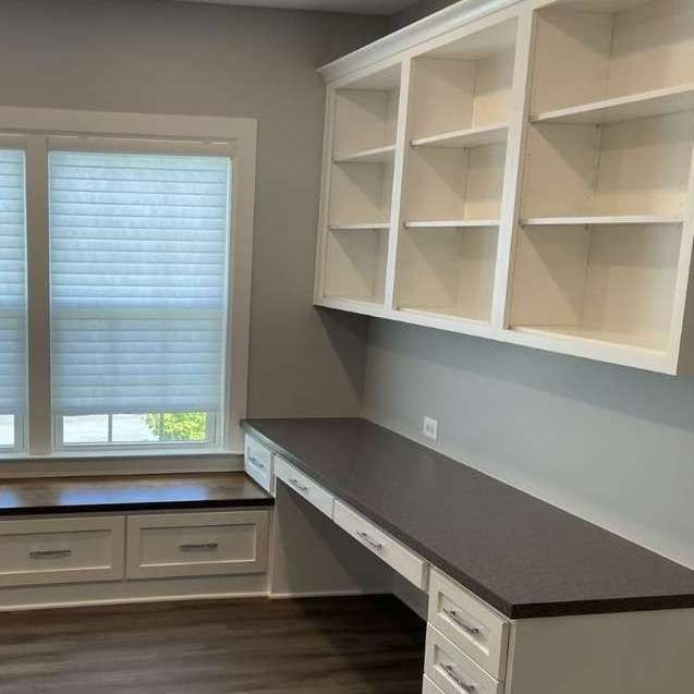 Built-in home office: white shelves and desk with dark countertop; window with seat below.