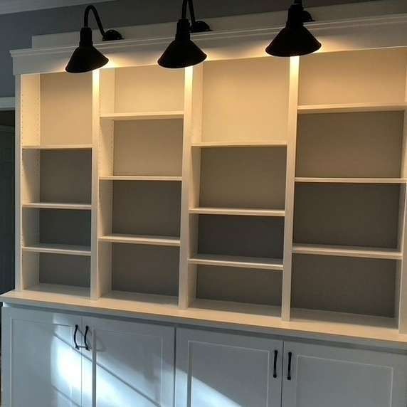 White built-in bookcase with four sections, above cabinets. Black spotlights are mounted above the shelves.
