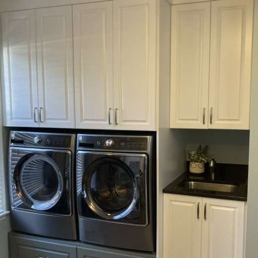 Laundry room with white cabinets above a washer and dryer, and a sink.