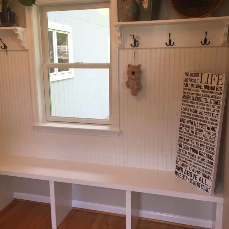 White built-in entryway bench with window, beadboard, and hooks. A sign with a quote hangs on the wall.