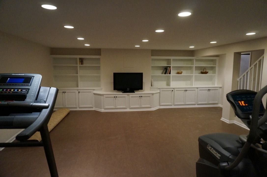 Home gym with treadmill, elliptical, built-in shelving, and a TV.