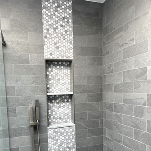 Gray tiled shower with mosaic accent and recessed shelves.