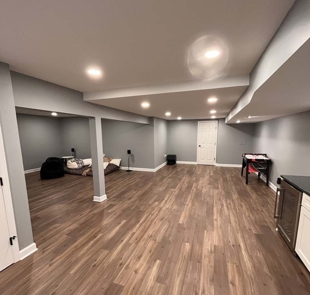 Spacious finished basement with hardwood floors, gray walls, and white trim. Includes a sofa, door, and music keyboard.