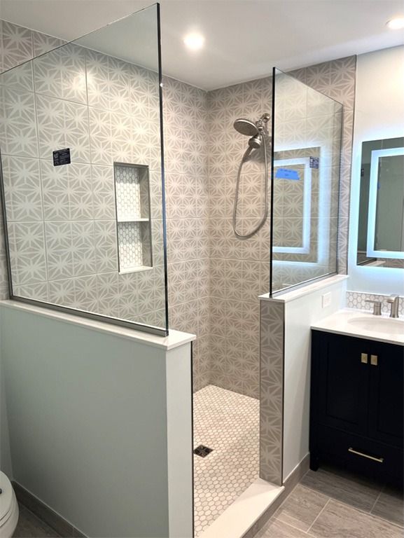 Bathroom shower with glass walls, tiled interior, and a built-in shelf. Blue vanity on the right.