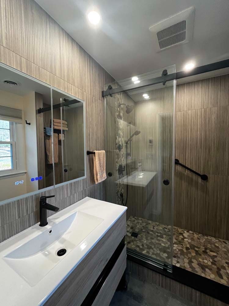 Modern bathroom with shower, vanity, and textured beige tile. Black fixtures and glass shower door.