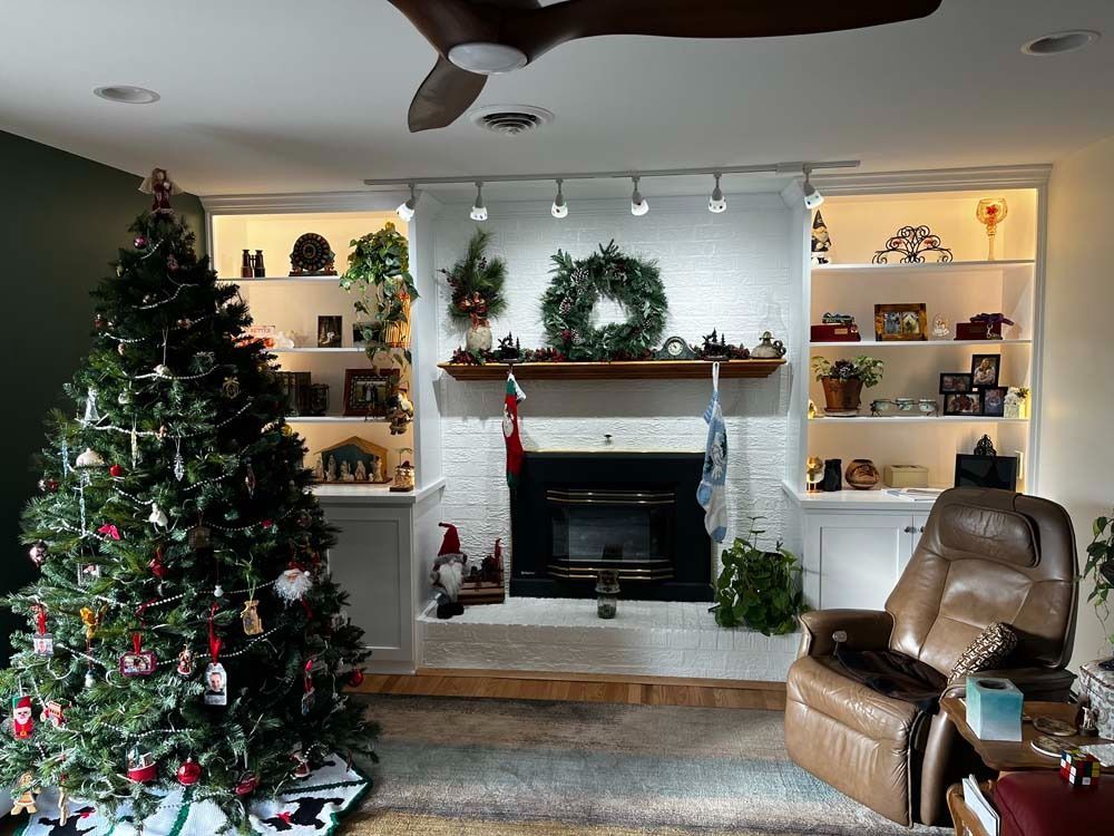 Christmas-decorated living room with a fireplace, built-in shelves, a recliner, and a tree.