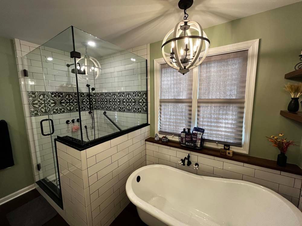 Modern bathroom: glass shower, white tub, dark accents, decorative tile, green walls, light fixture.
