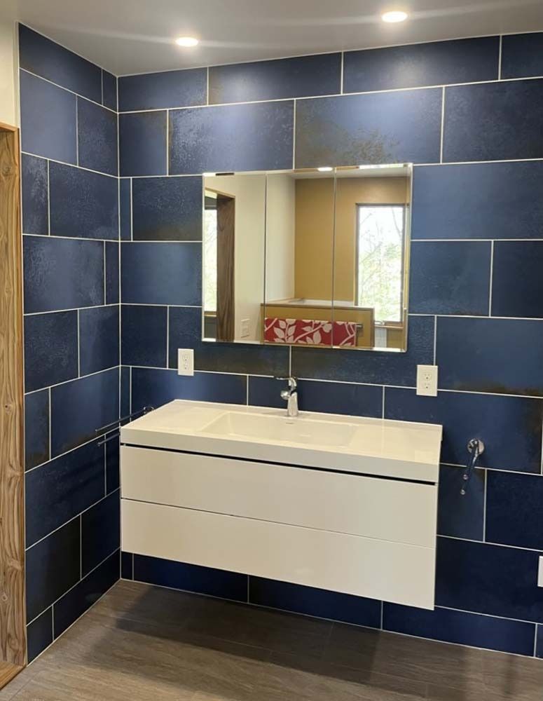 Modern bathroom with floating white vanity, dark blue tiled walls, and large mirror.