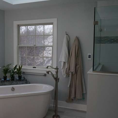 Bathroom with tub, shower, and window; two bathrobes hang on the wall.
