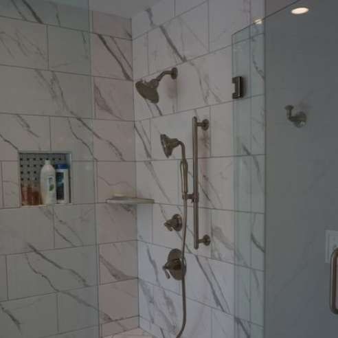 Shower with marble-look tile. Features a showerhead, handheld sprayer, and soap niche.