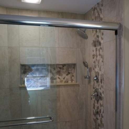 Shower with glass door, tiled walls in beige and mosaic accents, chrome fixtures.