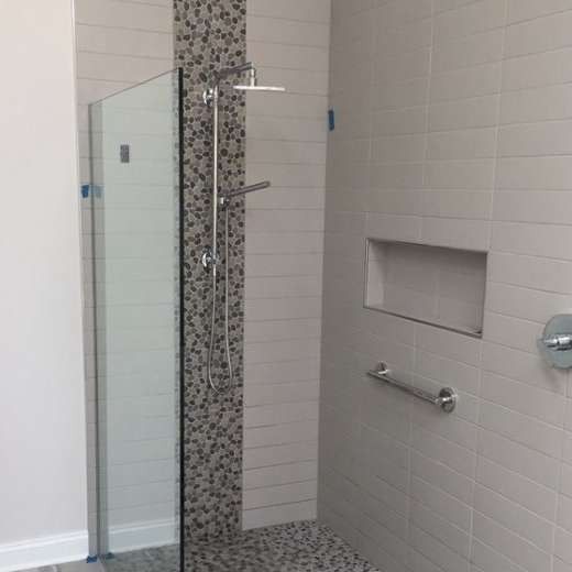 Accessible walk-in shower with glass door, mosaic tile accent, horizontal white tiles, recessed shelf, and grab bar.