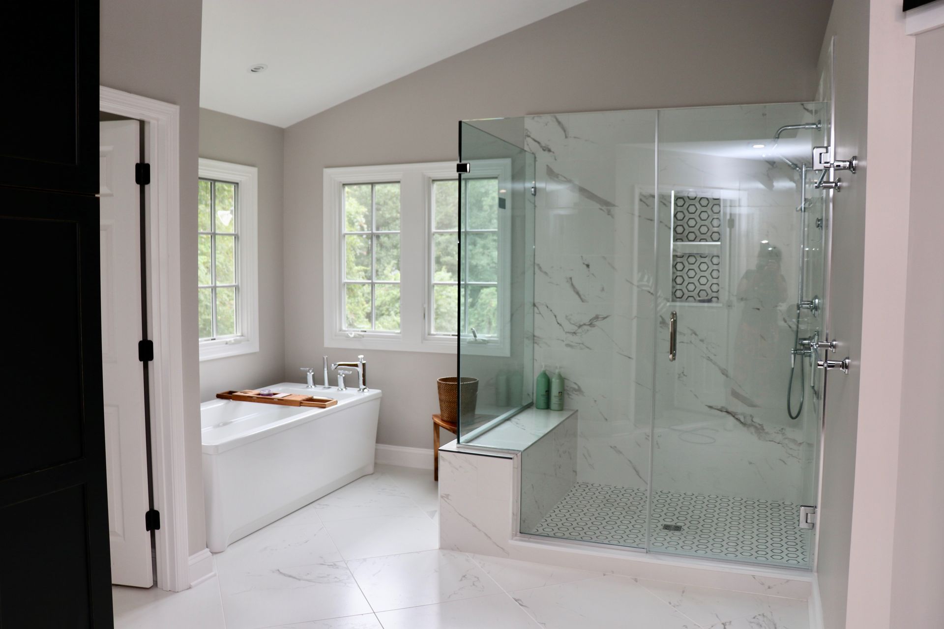 Spacious, bright bathroom with a white tub, glass shower, and marble-look tile.