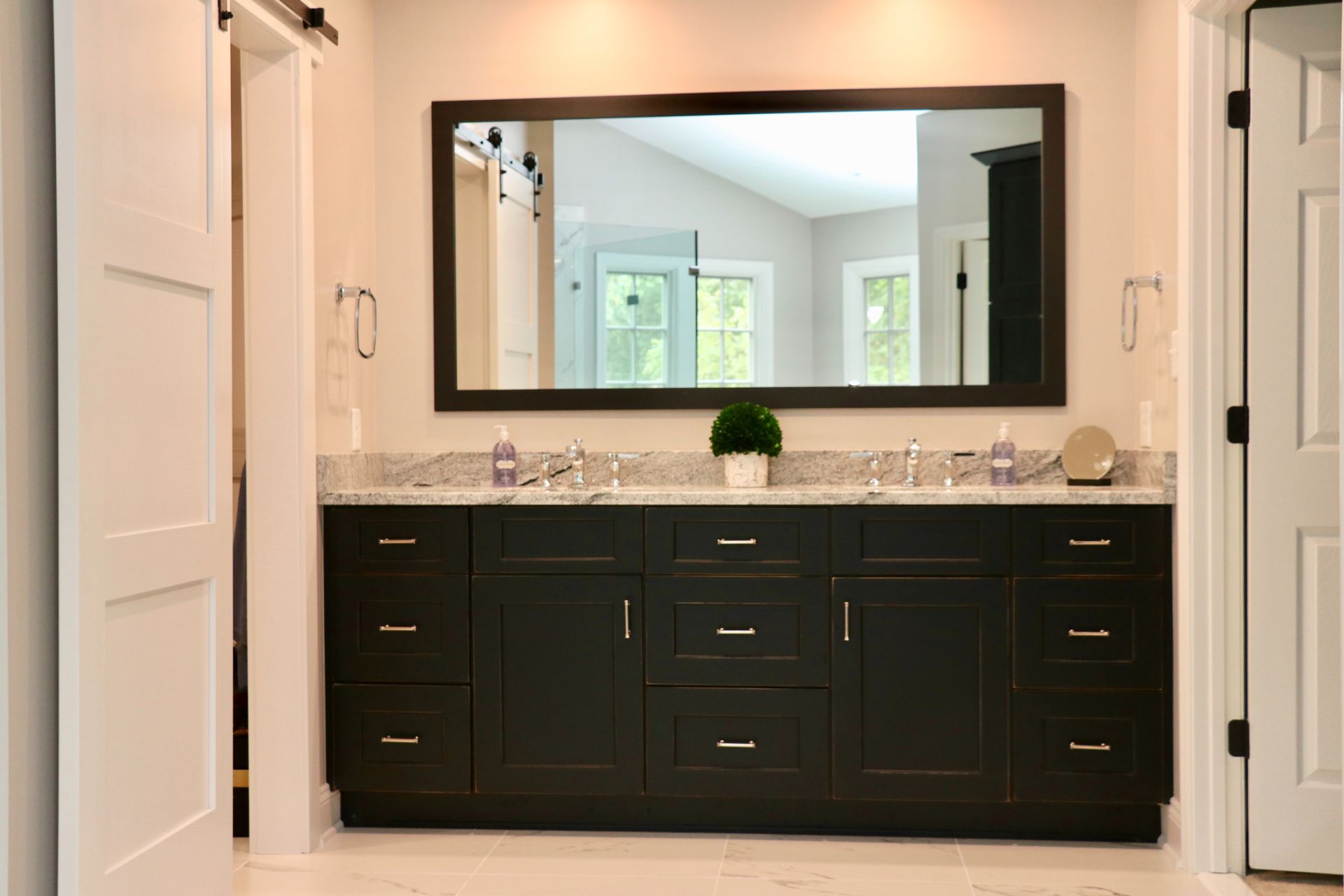Dark vanity with granite countertop, large mirror, and two sinks in a modern bathroom.