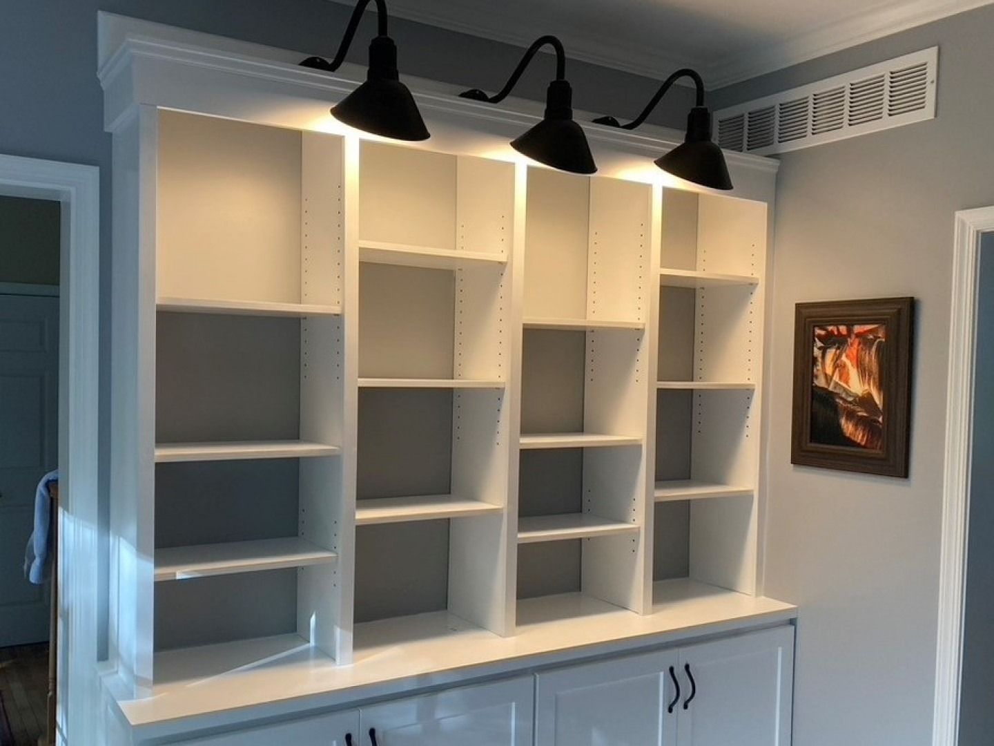White built-in shelves with overhead black lights, and a framed picture.