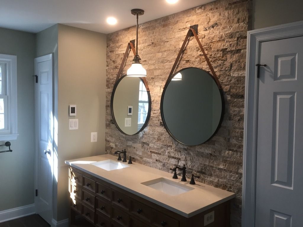 Bathroom with stone accent wall, two round mirrors, and a double vanity.