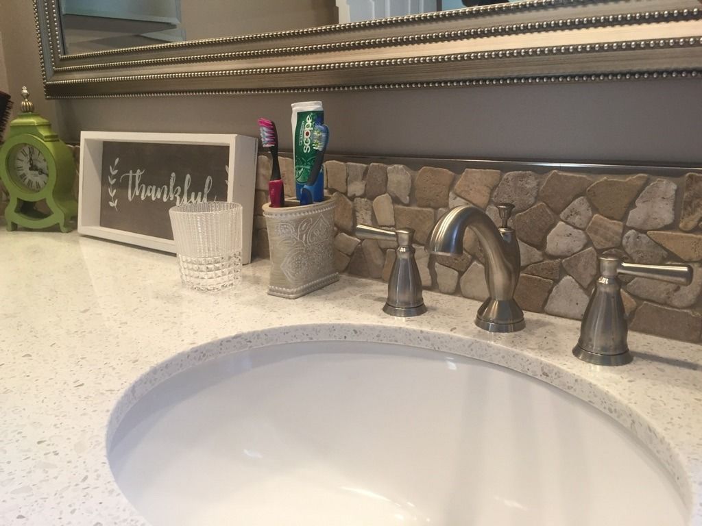 Bathroom countertop with a sink, faucet, toiletries, and a decorative mirror.