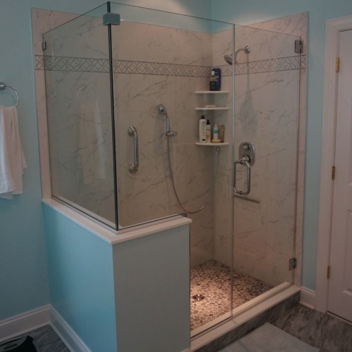Corner shower with glass doors, light marble walls, pebble floor, and built-in shelf; light blue walls.